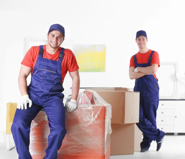 Trabalhadores do sexo masculino com caixas e móveis em casa nova — Fotografia de Stock