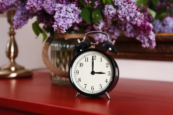 Alarm clock with lilac bouquet — Stock Photo, Image