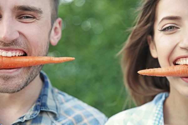 Przystojny mężczyzna i piękna dziewczyna jedzenia marchewki, zbliżenie — Zdjęcie stockowe