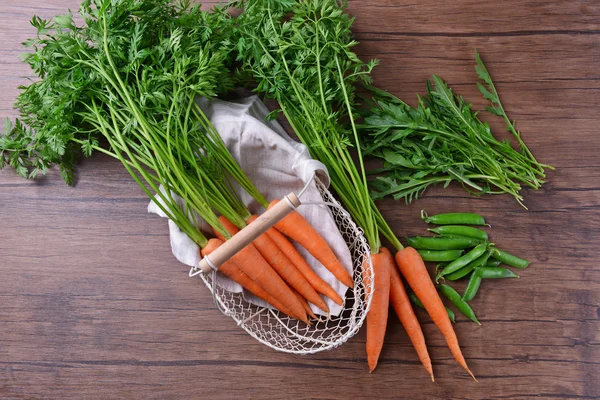 Wortel segar di keranjang wicker, kacang polong dan arugula — Stok Foto