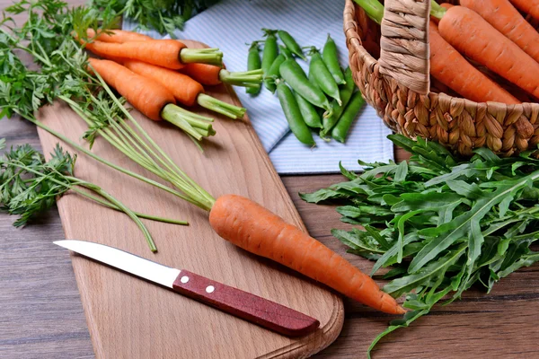 Fresh carrots in wicker basket, peas and arugula — Stock Photo, Image