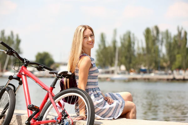 Девушка с велосипедом расслабляющий на берегу реки — стоковое фото