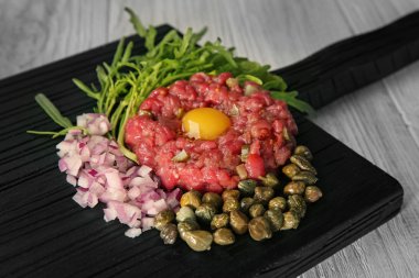 Biftek tartar kıyılmış onio ve bir tepsi üzerinde turşu ile