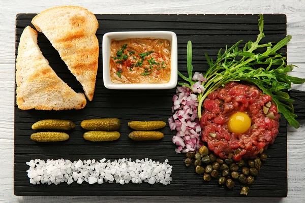 Biftek tartar kıyılmış onio ve bir tepsi üzerinde turşu ile