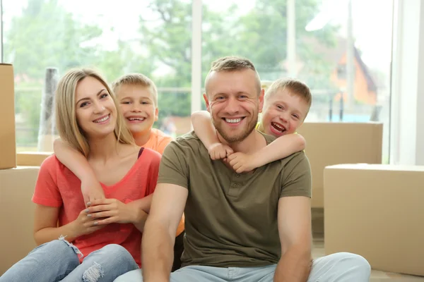 Gelukkige familie met kartonnen dozen zit op houten vloer — Stockfoto