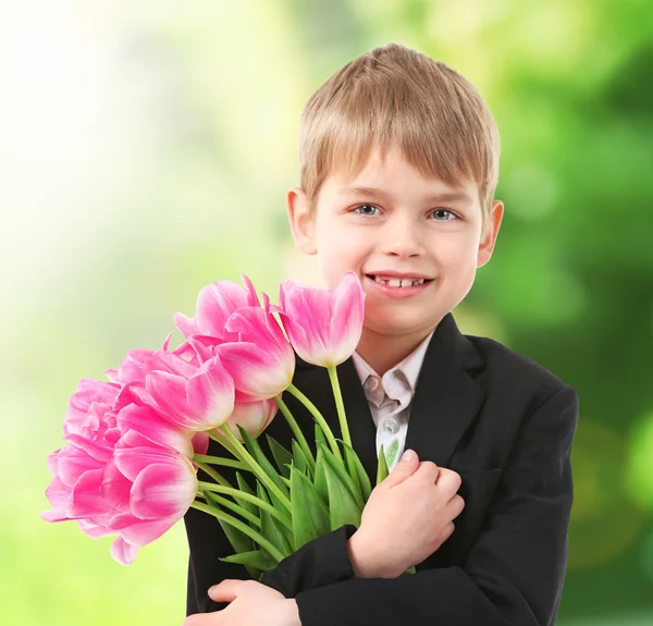 Χαριτωμένο αγόρι με λουλούδια σε θολή φόντο — Φωτογραφία Αρχείου