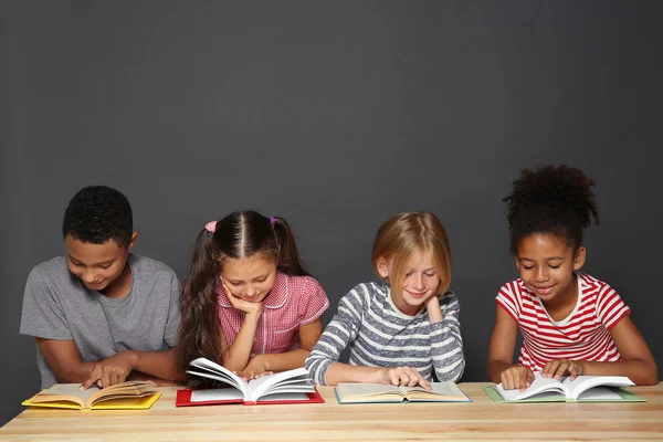 Милые дети читают книги на сером фоне — стоковое фото