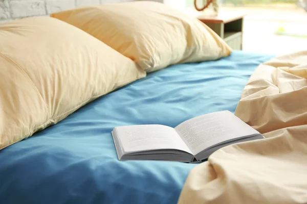 Opened book on crumpled bed — Stock Photo, Image