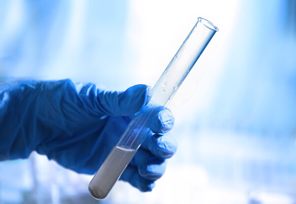 Hand in glove holding test tube with contaminated water