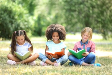 Yeşil çimenler üzerinde kitap okuyan sevimli çocuklar.