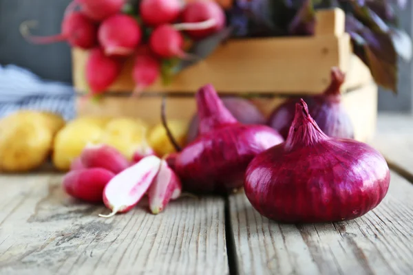 Fresh onion and crate with vegetables on wooden table — Stock Photo, Image