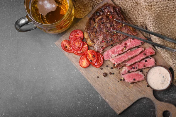 Gesneden smakelijke biefstuk met tomaten en bier op de snijplank — Stockfoto