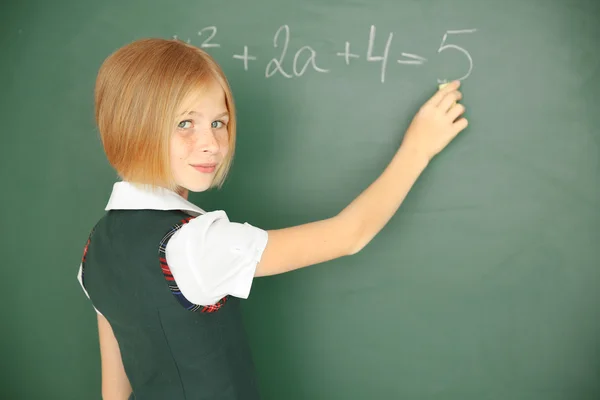 Schoolgirl writing on chalkboard — Stock Photo, Image