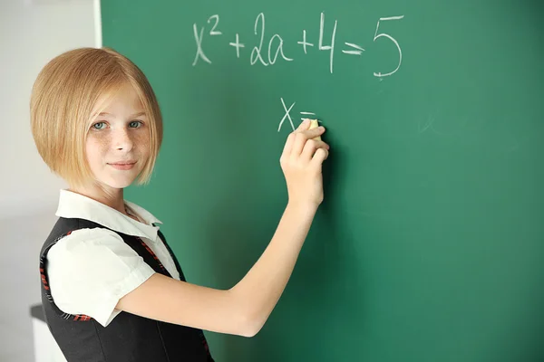 Schoolgirl writing on chalkboard — Stock Photo, Image