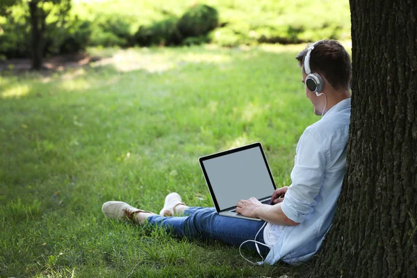 Man with laptop listening music in park — Stock Photo, Image