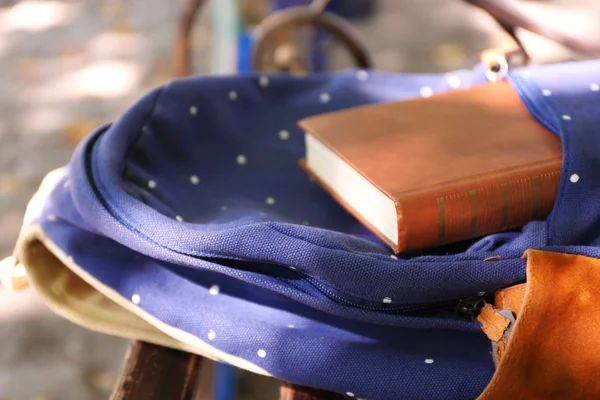 Backpack and book on bench — Stock Photo, Image