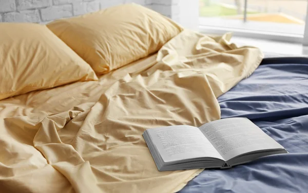 Aufgeschlagenes Buch über zerknittertes Bett im Zimmer — Stockfoto