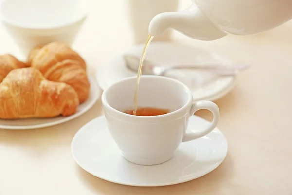 Verter té en taza y croissants — Foto de Stock