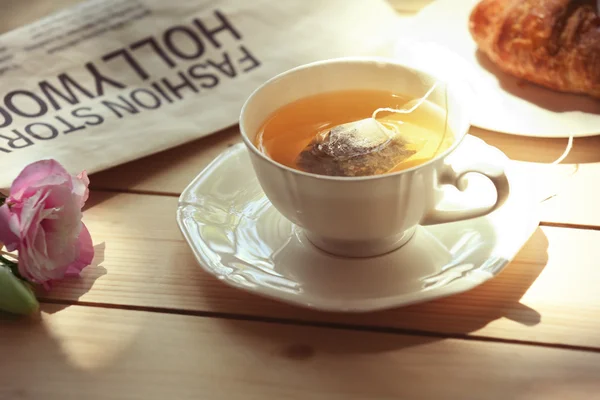 Cup of tea with croissant and newspaper — Stock Photo, Image