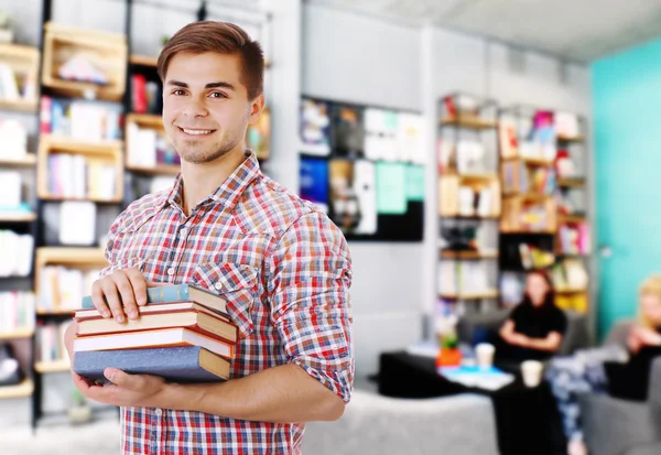 Young man with stack of books on blurred book shelves background.