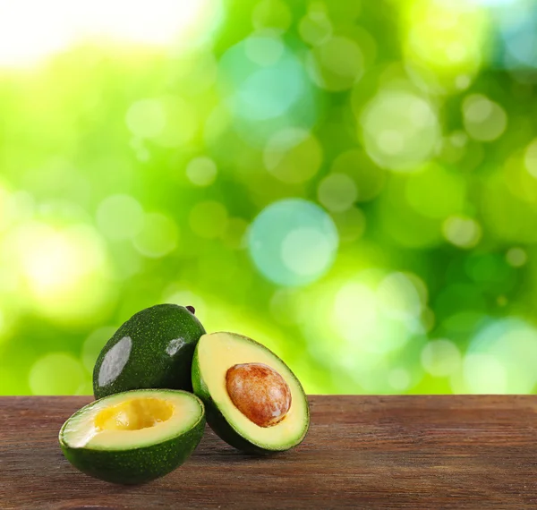 Fresh avocados on wooden table. Blurred green background. — Stockfoto