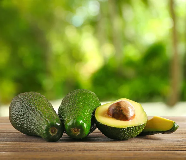 Aguacates frescos sobre mesa de madera. Fondo verde borroso . — Foto de Stock