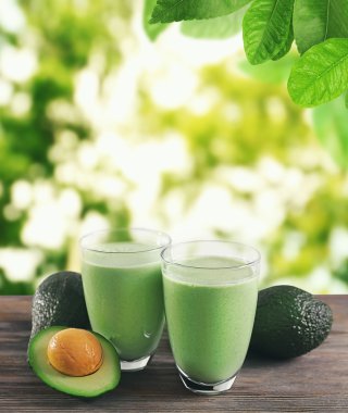 Avokado ahşap masaya kokteyl gözlüklü. Yeşil arka plan bulanık.