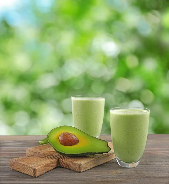 Verres avec cocktail d'avocat sur table en bois. Fond vert flou . — Photo