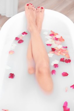 Woman legs with flower petals in bathtub clipart
