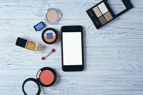Dekoratív kozmetikumok és smartphone fából készült háttér — Stock Fotó