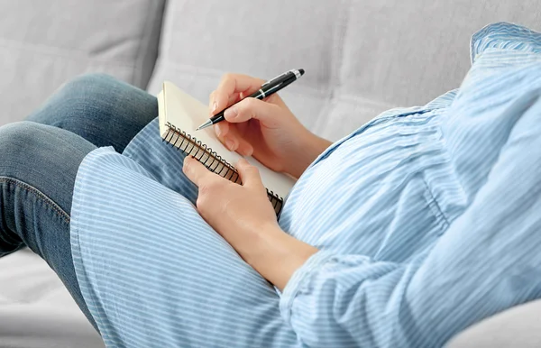 Gravid kvinna skriva i anteckningsboken och sitter på soffa — Stockfoto