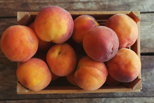 Fresh peaches in a box on a wooden background — Stock Photo, Image