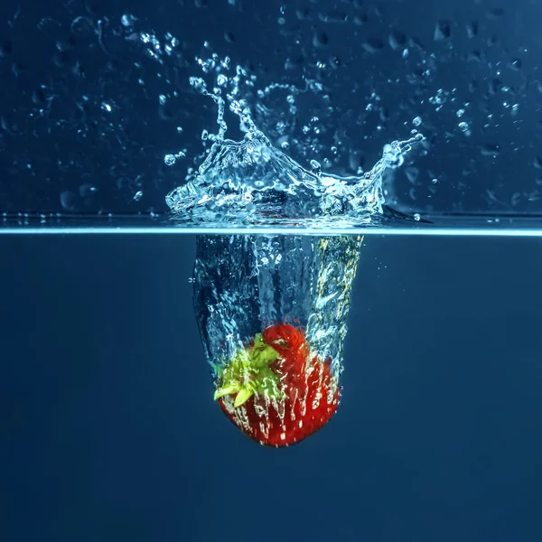 Frische saftige Erdbeere fällt ins Wasser auf dunklem Hintergrund — Stockfoto
