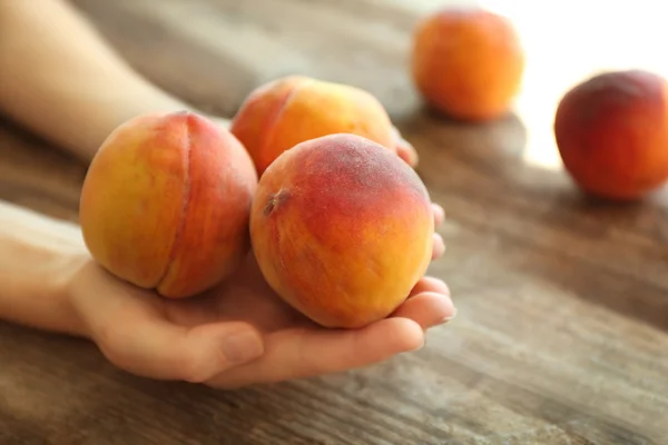 Vrouwelijke handen bedrijf verse perziken op een houten achtergrond — Stockfoto