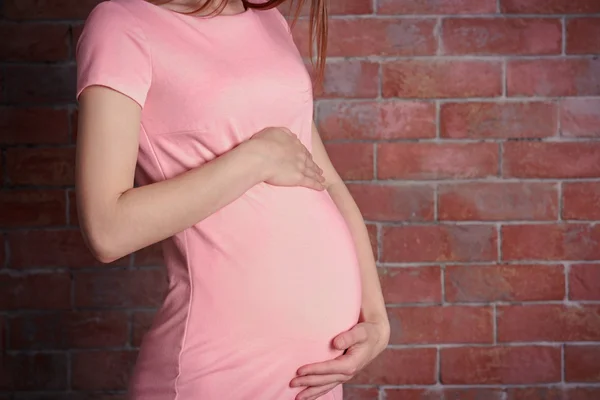 Pregnant woman on brick wall background, close up — Stock Photo, Image