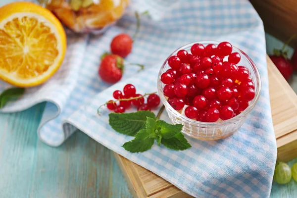 Fresh red currant and orange in glass bowl on wooden box — Stock fotografie