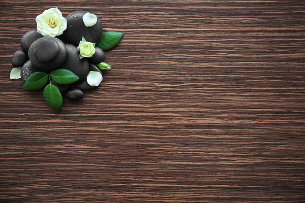 Spa stones with rose and petals on wooden background