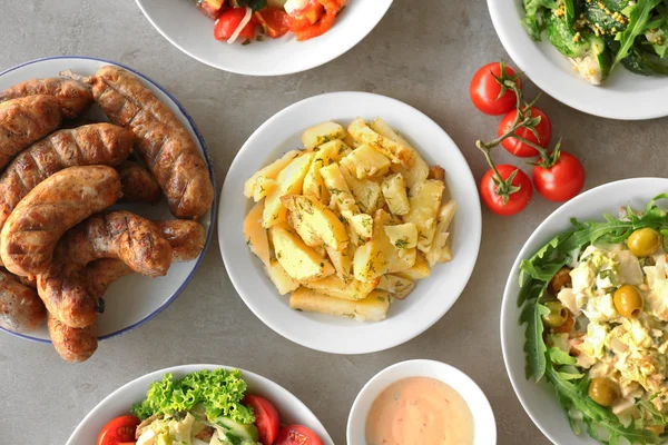 Plates with fried potato, sausages and salads on table — Stock Photo, Image