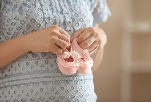 Kobieta w ciąży, trzymając dziecko różowe buciki — Zdjęcie stockowe