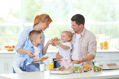 Mutlu bir aile mutfakta pizza yiyor.