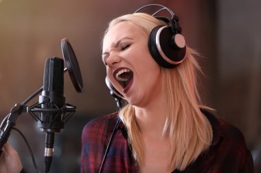 Genç bir kadın profesyonel bir stüdyoda şarkı kaydediyor.