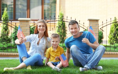 Mutlu aile evlerinin yanında çimenlerin üzerinde oturan küçük Amerikan bayrakları ile