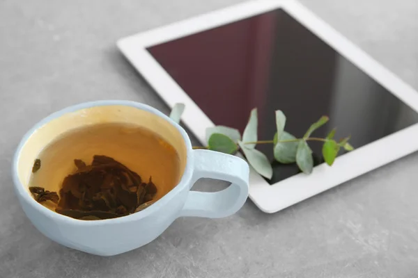 Tablet, leaves and cup of tea on a grey table — Stock Photo, Image