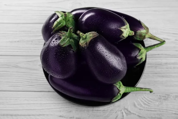 Plate with fresh aubergines on wooden background, top view — Stock Photo, Image