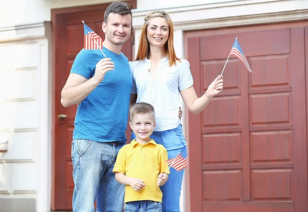 Família feliz com pequenas bandeiras americanas ao lado da porta de casa — Fotografia de Stock