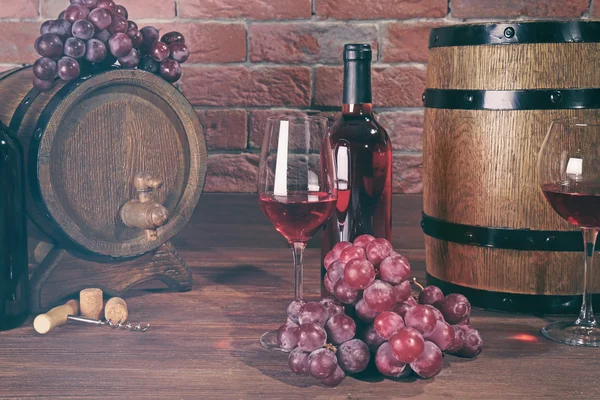 Glazen rode wijn, druiven en houten vaten op een bakstenen muur achtergrond — Stockfoto