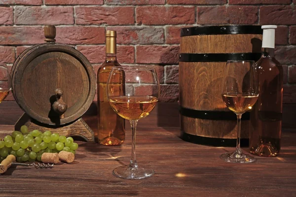 Bicchieri di vino bianco, uva e botti di legno su uno sfondo muro di mattoni — Foto Stock