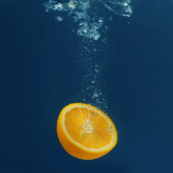 De helft van vers sappige oranje vallen in water op donkere achtergrond — Stockfoto