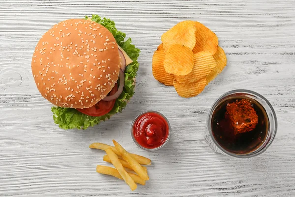 Tasty cheeseburger with snack and coke on wooden table — Stock Photo, Image