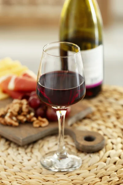 La copa con el vino tinto y los tentempiés sabrosos en la tabla sobre la estera de mimbre — Foto de Stock